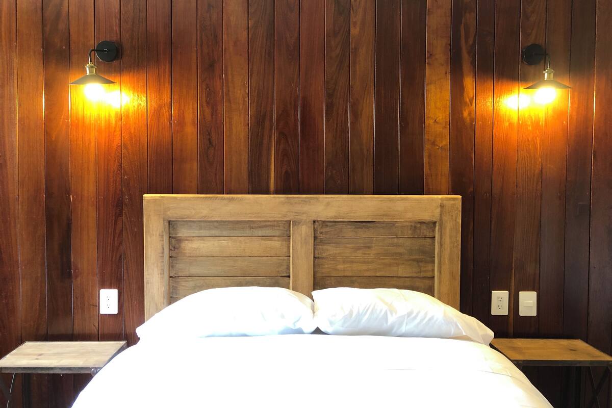 A wooden-paneled room with a bed, two nightstands, and wall-mounted lights.
