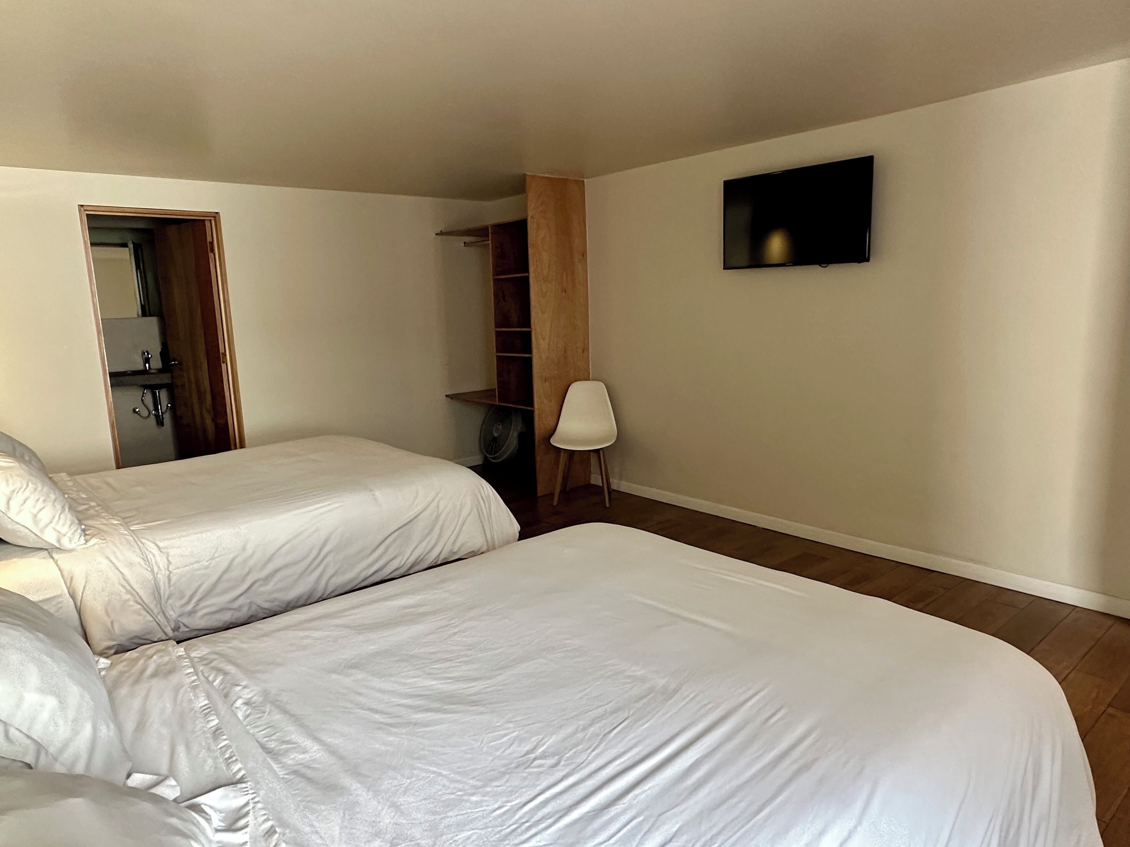 Une chambre avec deux lits, une armoire en bois, une chaise et un téléviseur fixé au mur.