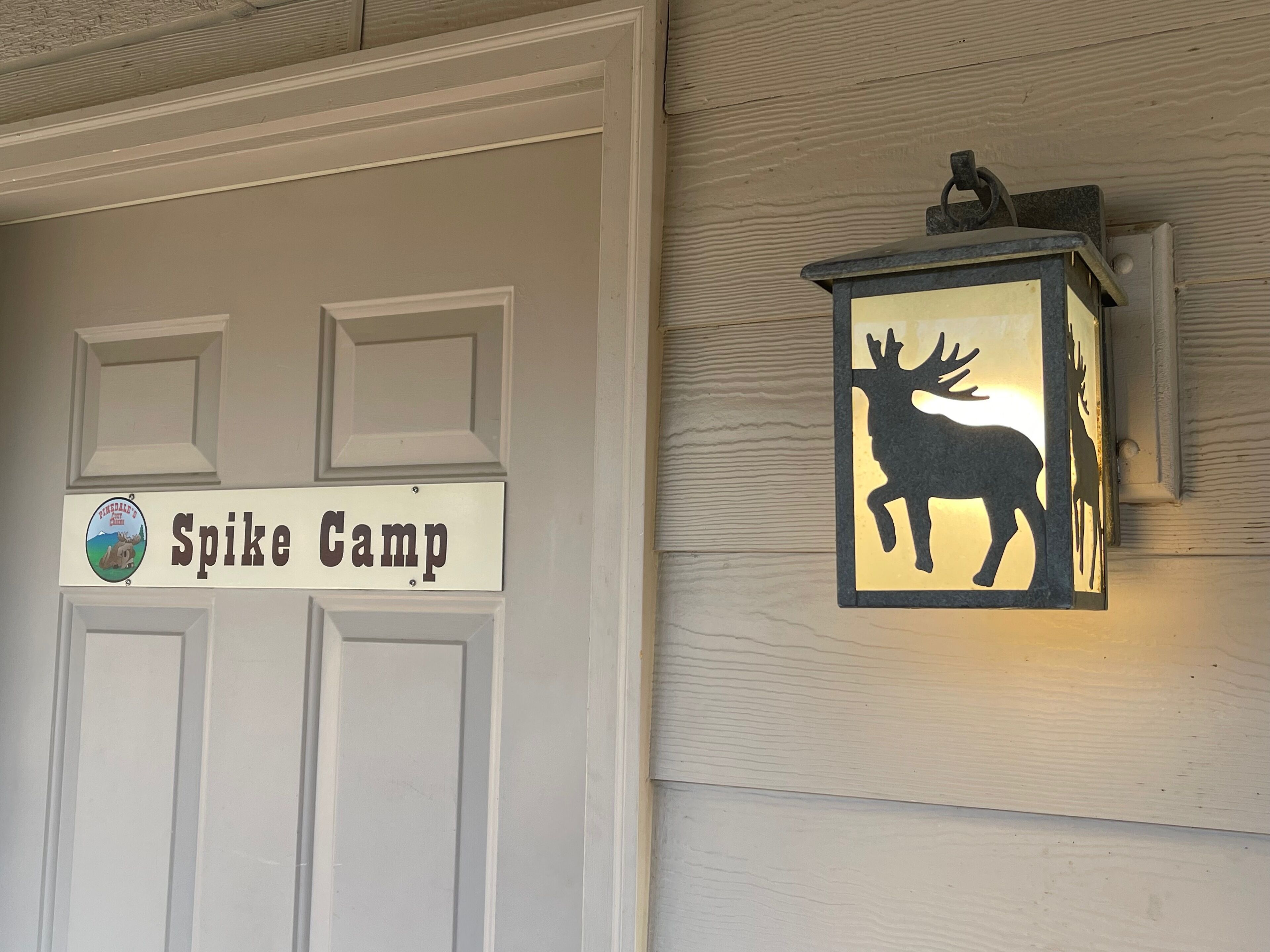 A door with a sign reading "Spike Camp" and a mounted lantern with a silhouette of a deer.