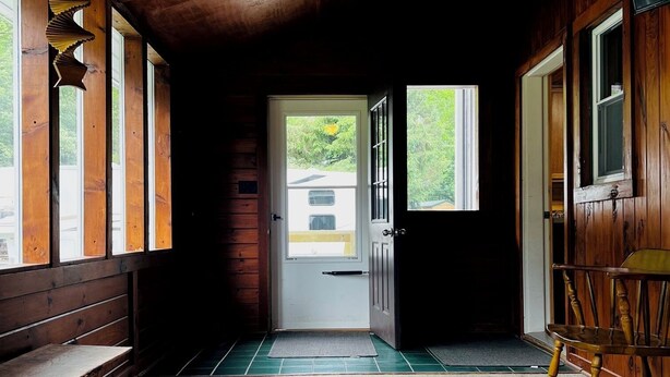 A wooden interior with a ceiling fan, a bench, a rug, and a door leading outside.