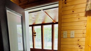 A wooden cabin interior with a door leading to a porch, a bench, and a countertop with a sink.