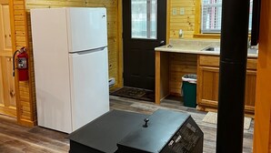 A compact kitchen with wooden walls, a white refrigerator, a black stove, and a window with blinds.