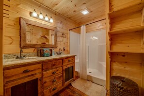 Ein Badezimmer in einer Holzhütte mit einem Holzwaschtisch, einem Spiegel, einer Duschvorhang und einem kleinen gewebten Korb.