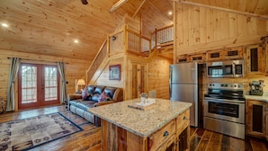 A wooden cabin interior with a living area, kitchen, and a staircase leading to an upper level. - LOG CABIN + MOUNTAIN VIEWS! HOT TUB, POOL & GAME TABLE, FIBER WIFI & DISCOUNTS! (Murphy)