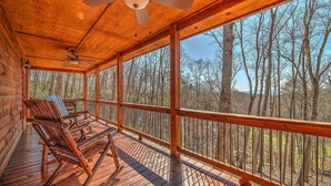 A wooden deck with rocking chairs and a ceiling fan, overlooking a forested area. - LOG CABIN + MOUNTAIN VIEWS! HOT TUB, POOL & GAME TABLE, FIBER WIFI & DISCOUNTS! (Murphy)