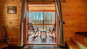 A wooden cabin with a deck, rocking chairs, and a table. - LOG CABIN + MOUNTAIN VIEWS! HOT TUB, POOL & GAME TABLE, FIBER WIFI & DISCOUNTS! (Murphy)