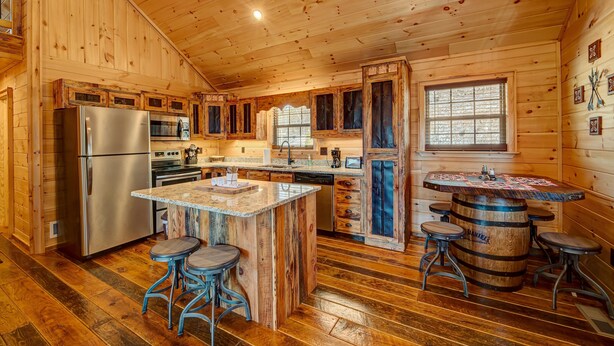 A wooden cabin kitchen with a central island, bar stools, a refrigerator, and a window. - LOG CABIN + MOUNTAIN VIEWS! HOT TUB, POOL & GAME TABLE, FIBER WIFI & DISCOUNTS! (Murphy)