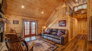 A wooden cabin interior with a leather sofa, a rocking chair, a staircase, and a fireplace. - LOG CABIN + MOUNTAIN VIEWS! HOT TUB, POOL & GAME TABLE, FIBER WIFI & DISCOUNTS! (Murphy)
