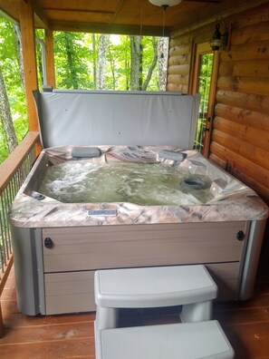 Ein Whirlpool mit einem marmorähnlichen Deckel, eine Holzterrasse und Blick auf Bäume.