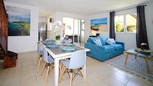 Un salon moderne avec un coin repas, comprenant un canapé bleu, une table à manger dressée avec des assiettes et des verres, et une cuisine en arrière-plan.