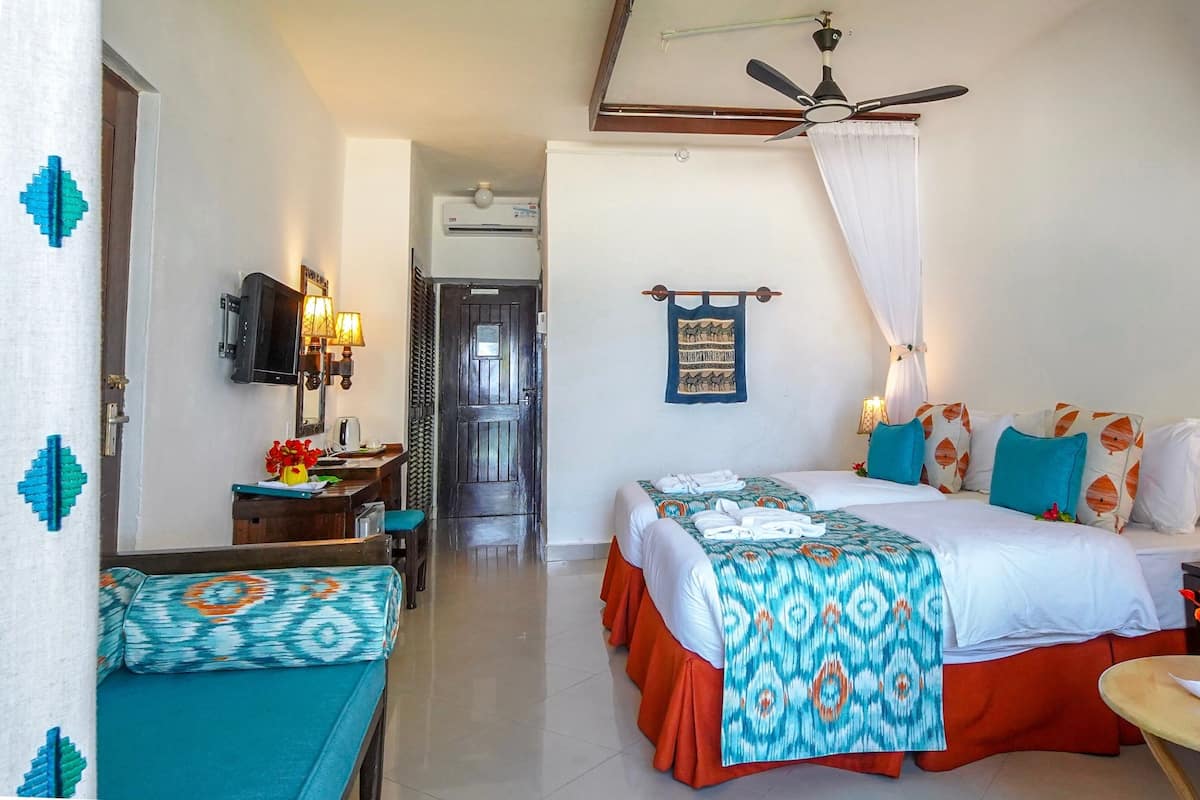 Habitación de hotel con cama, escritorio, silla, mesa con un florero y ventilador de techo.