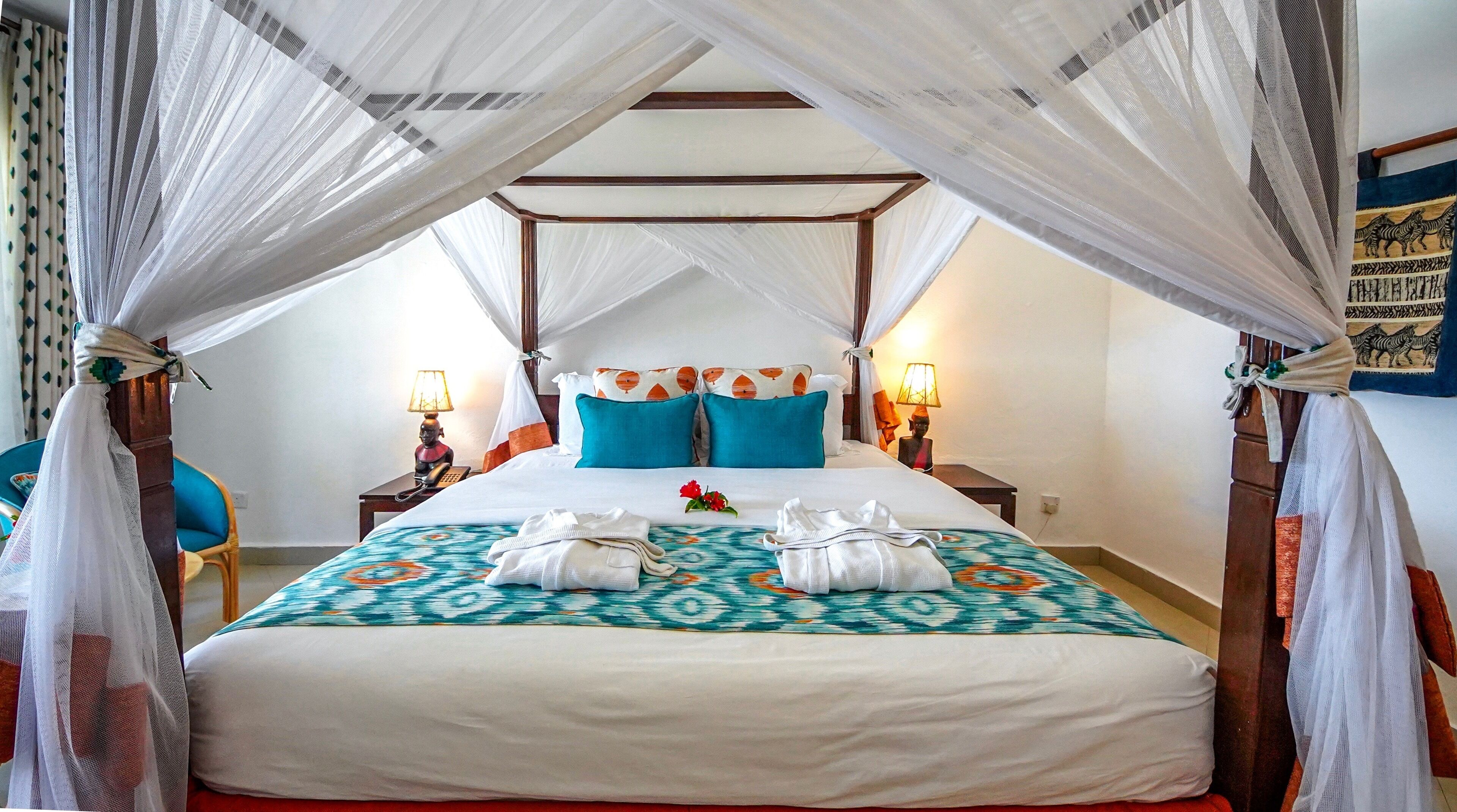 A bed with a canopy, two nightstands, a chair, and a wall with a painting.