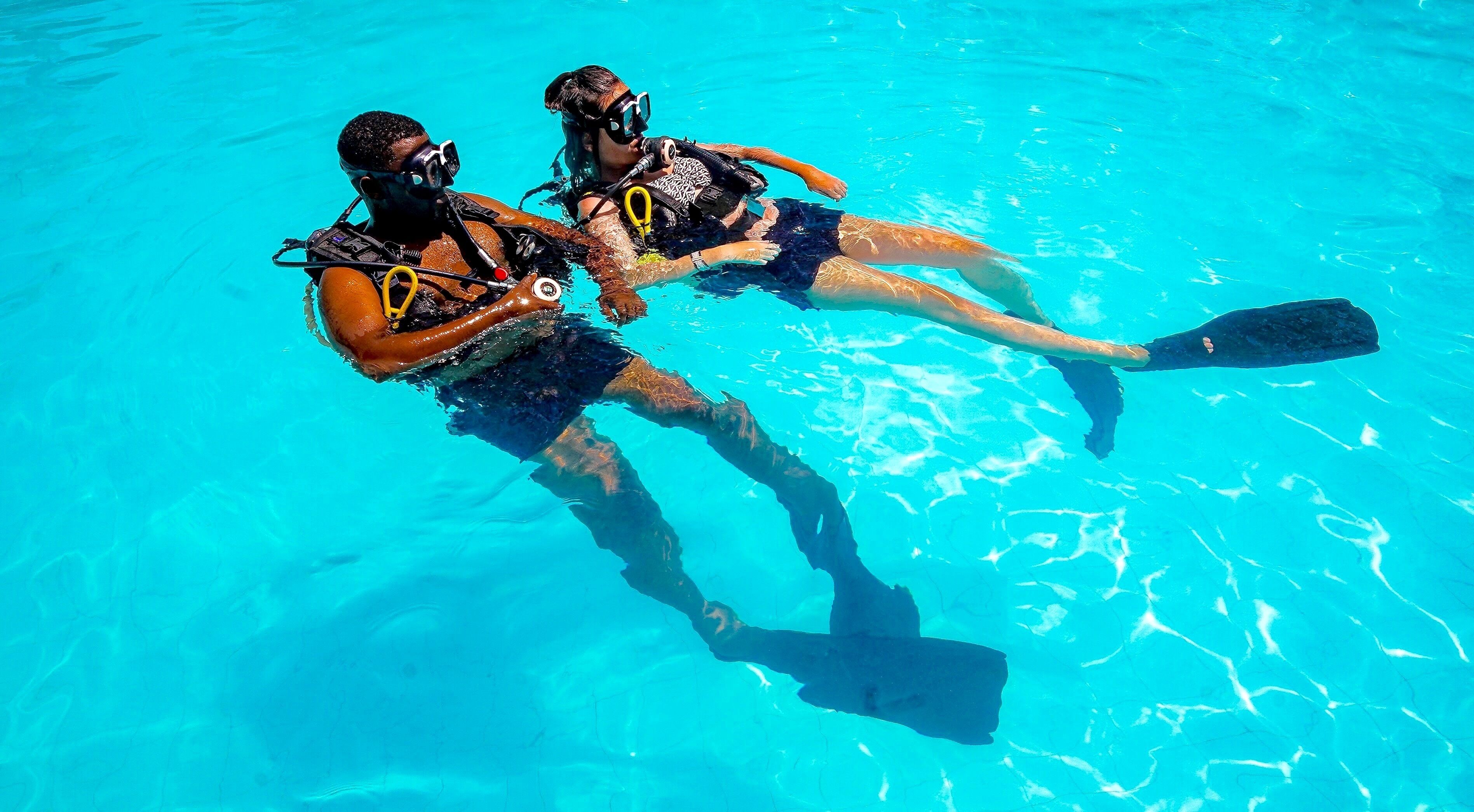 Two people in a clear blue pool, wearing scuba diving gear.