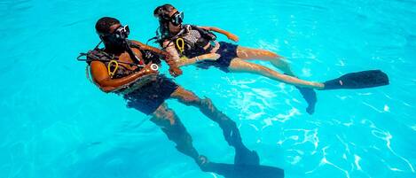 Two people in a clear blue pool, wearing scuba diving gear.
