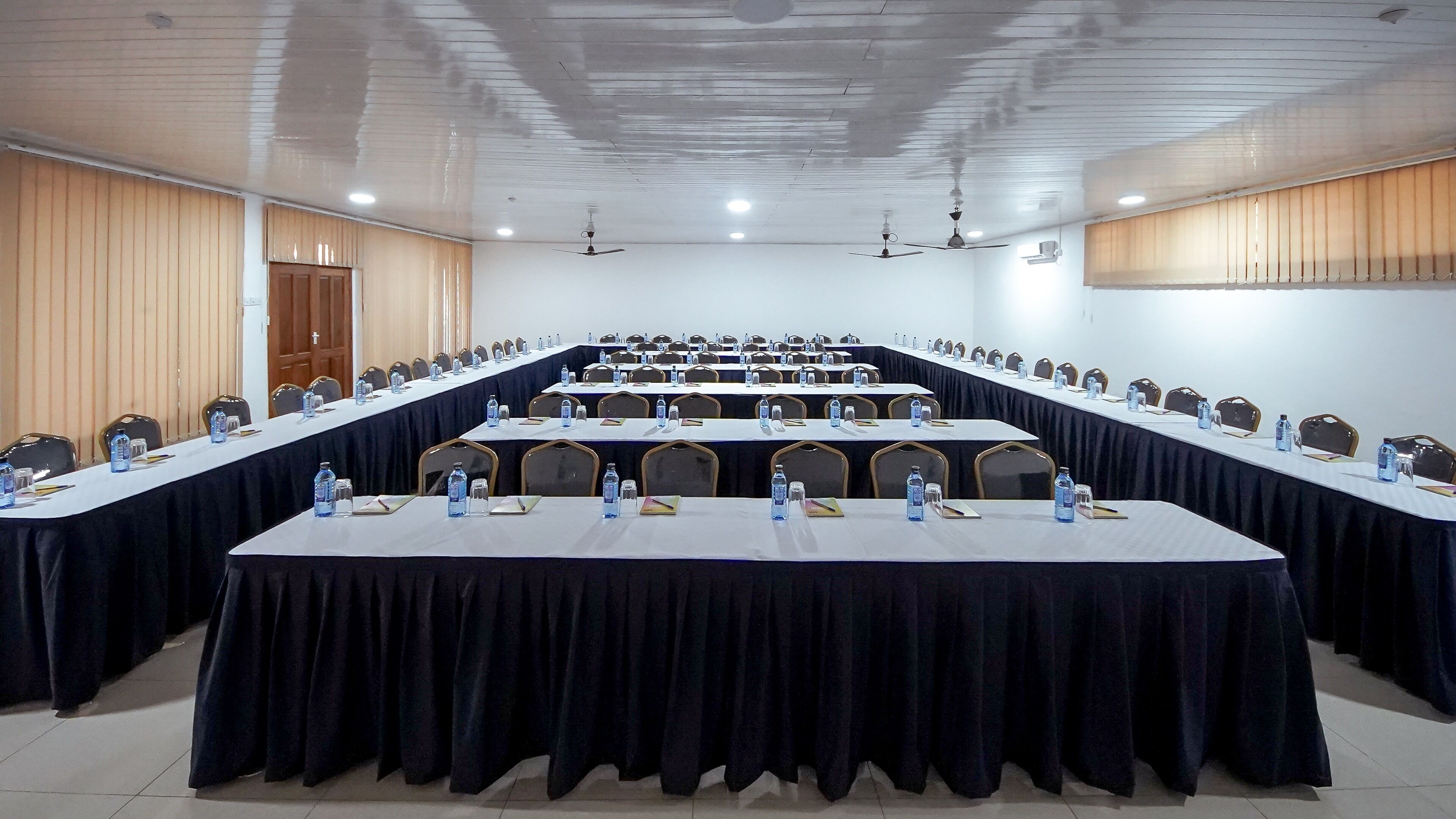 A conference room with multiple tables, chairs, and ceiling fans.