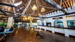 An indoor reception area with a stone floor, reception desk, and seating area with benches. - Papillon Lagoon Reef (Diani Beach)