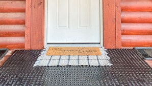 A wooden cabin door with a white panel, a welcome sign, a horse's head emblem, and a pair of boots on the right. - Cozy and secluded Log Cabin near the Frio River with a private pool! (Concan)