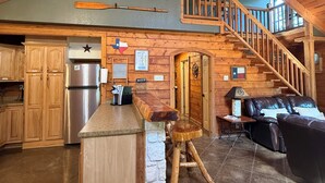 A spacious kitchen with wooden cabinets, a large island, and a stainless steel refrigerator. - Cozy and secluded Log Cabin near the Frio River with a private pool! (Concan)