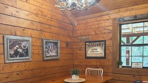 A wooden dining room with a chandelier, framed pictures, and a window with a view. - Cozy and secluded Log Cabin near the Frio River with a private pool! (Concan)