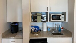 Une petite cuisine équipée d’un four à micro-ondes, d’un grille-pain et d’une machine à café. On y trouve deux placards blancs au-dessus du plan de travail, ainsi qu’un petit évier avec un robinet.