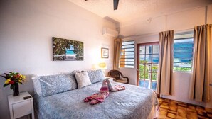 Un dormitorio con cama, mesita de noche, silla, ventana con cortinas y un cuadro en la pared.