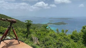 A wooden deck with a telescope overlooking a coastal landscape with clear blue waters and islands.