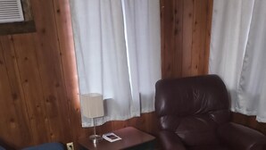 Una habitación con un sofá azul, un sillón de cuero, una mesita con una lámpara y cortinas.