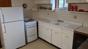 Una cocina compacta con electrodomésticos blancos, un ventanal y un lavamanos.