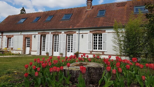 Un edificio tradicional con tejado de tejas, ventanas de tejado y un jardín con tulipanes rojos.