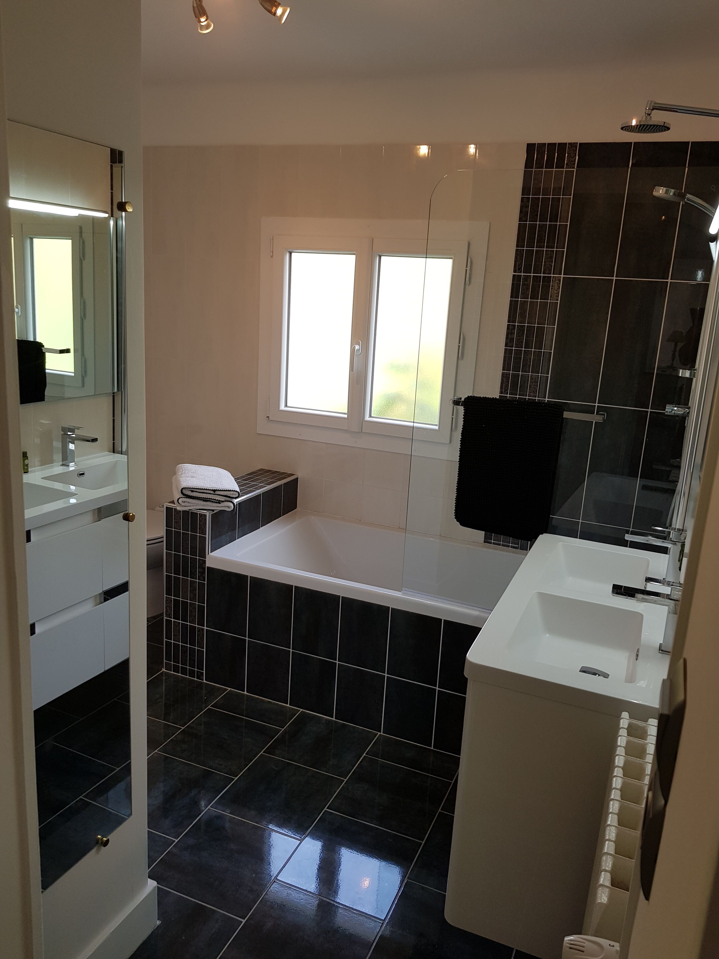A modern bathroom with a bathtub, two sinks, a large mirror, and a window.