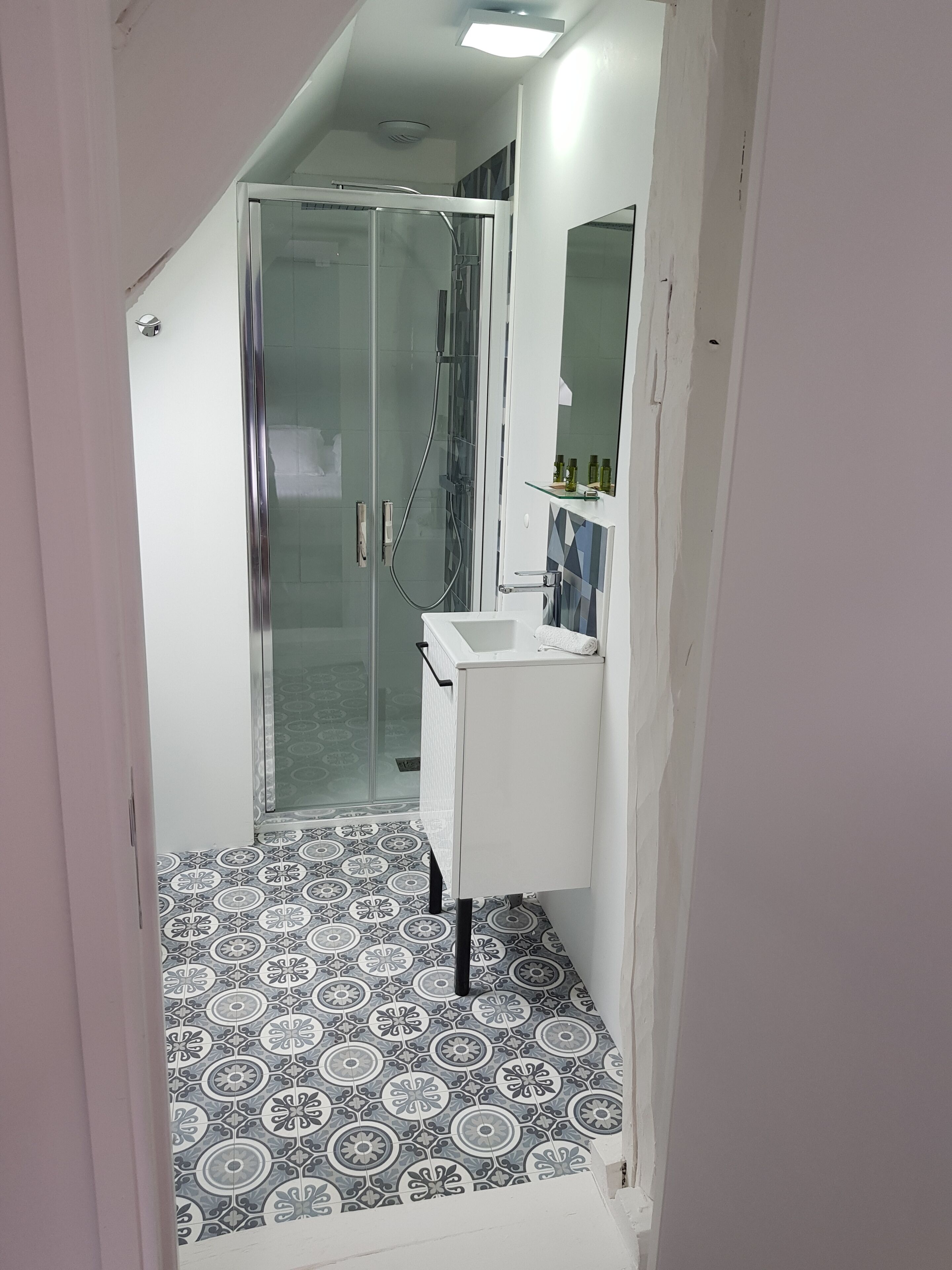A narrow hallway leading to a bathroom with a shower, a sink, and a mirror.