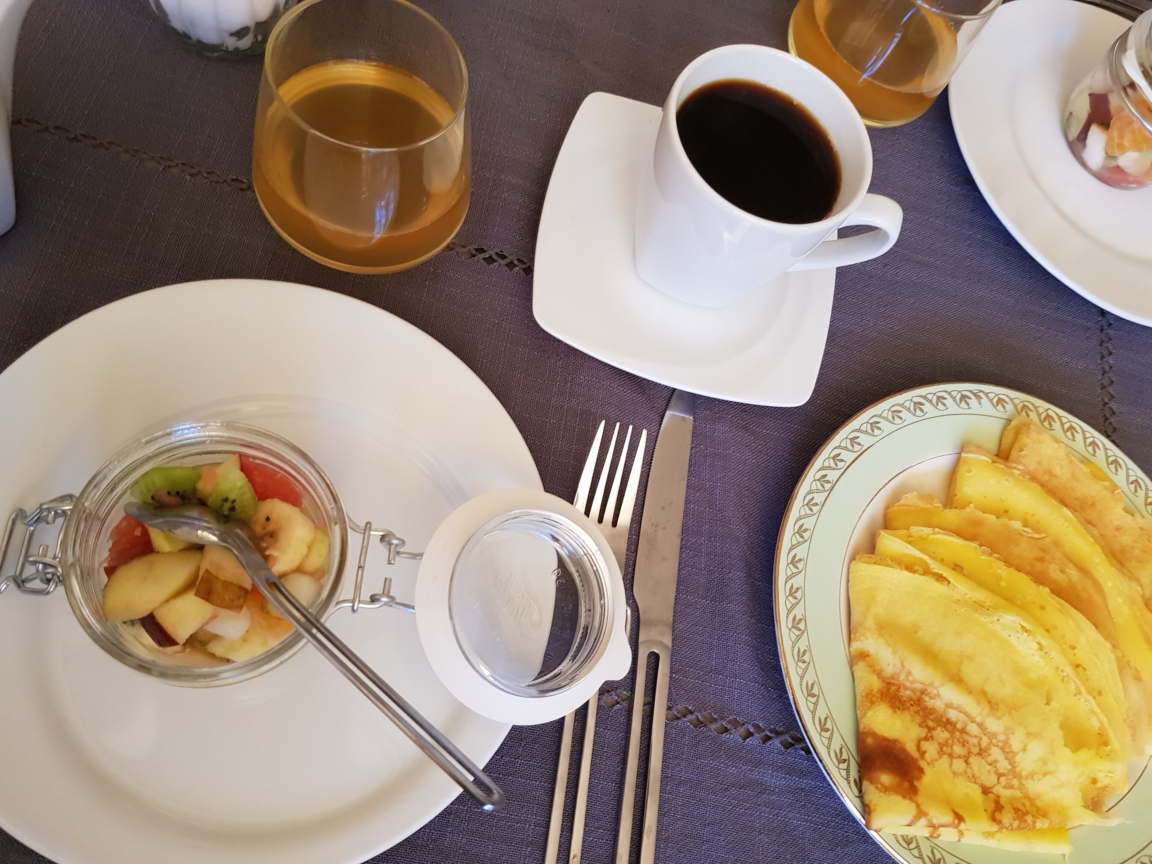 A table set with plates of food, a glass of tea, a cup of coffee, and cutlery.