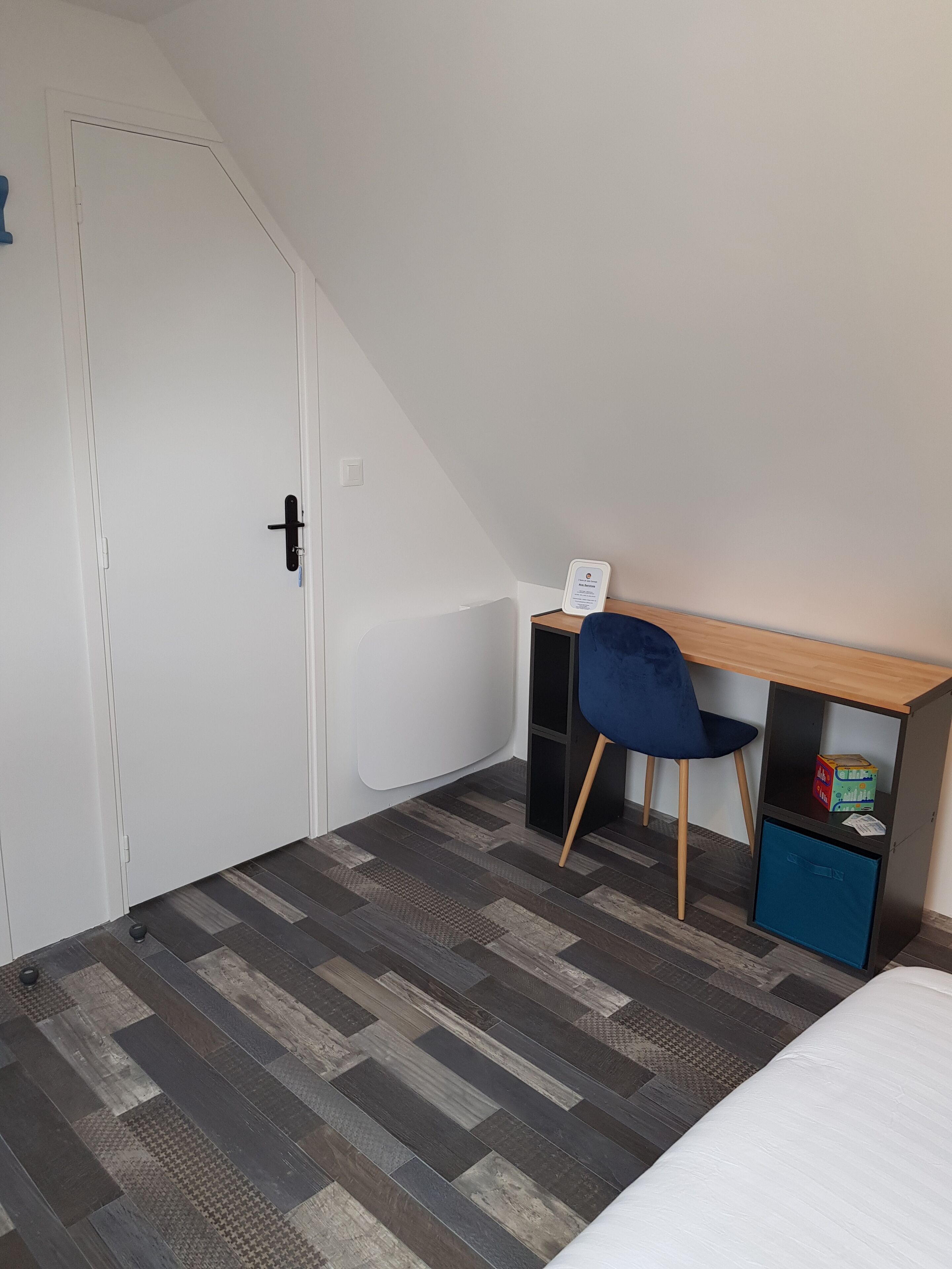 A small room with a bed, a desk with a chair, a wardrobe, and a door.