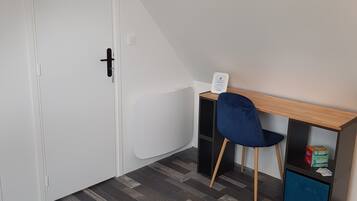 A small room with a bed, a desk with a chair, a wardrobe, and a door.
