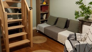 Una sala de estar acogedora con una escalera de madera, un sofá, una estantería y una lámpara colgante.