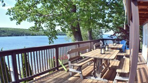 Una terraza de madera con mesas de picnic y bancos, con vista a un lago.