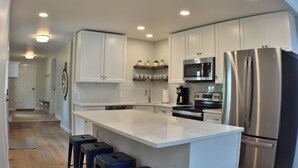 Cocina moderna con armarios blancos, una isla grande con taburetes de bar, electrodomésticos de acero inoxidable e iluminación empotrada en el techo.
