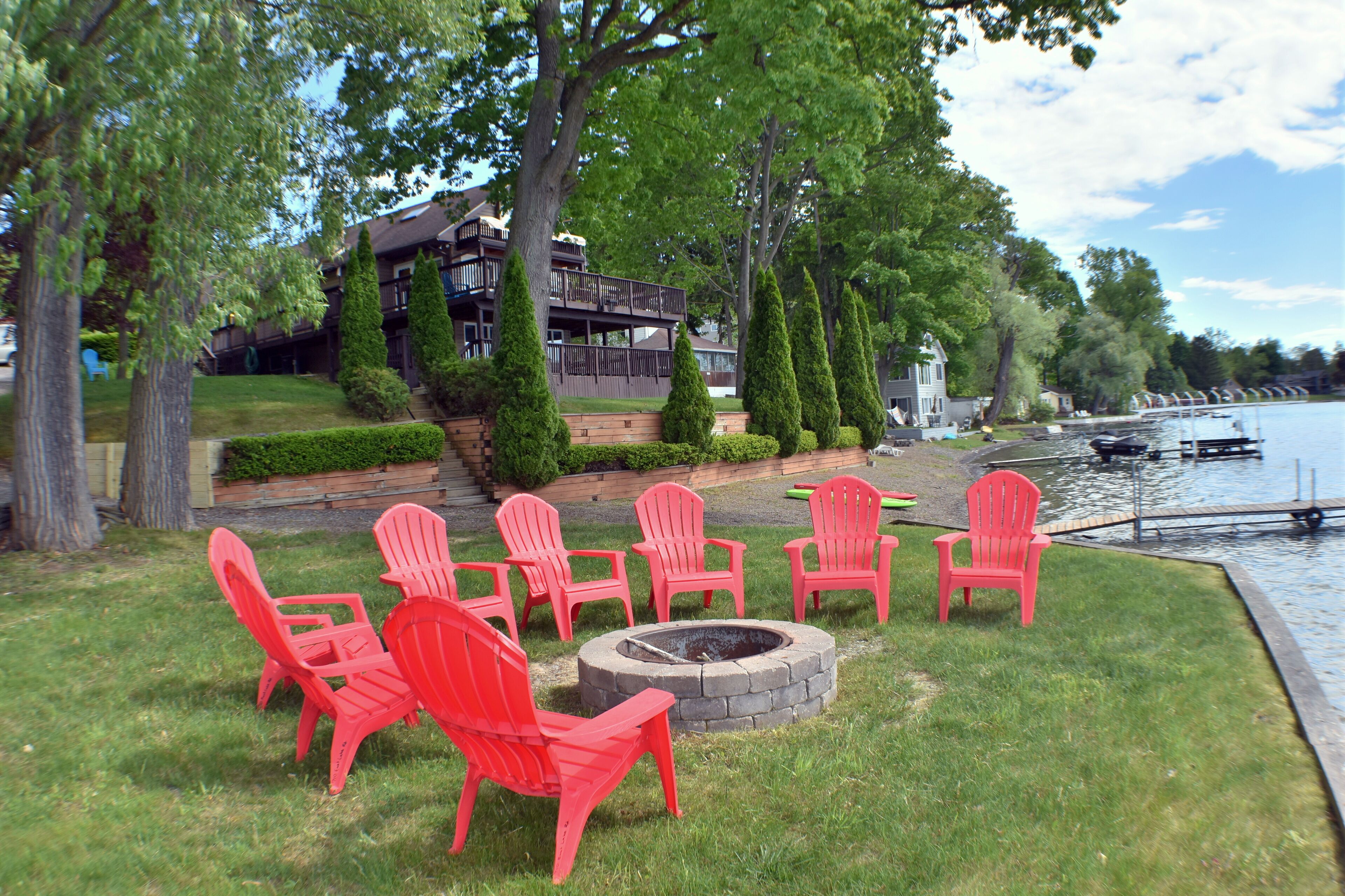 A lakeside setting with a fire pit and red Adirondack chairs.