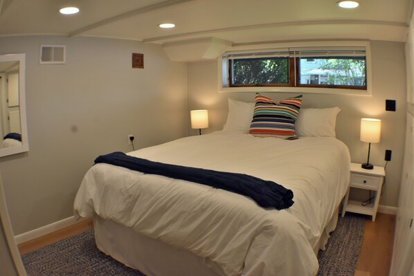 A bedroom with a large bed, two bedside lamps, a window with a view, and a small bedside table.