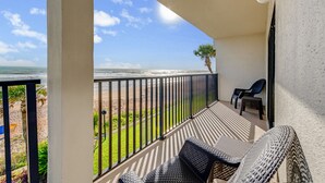Un balcón con vista al océano, una palmera y mobiliario exterior.