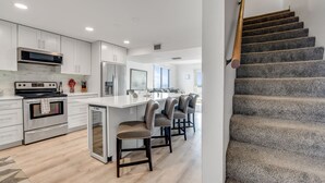 Una cocina moderna con armarios blancos, electrodomésticos de acero inoxidable y una isla central con taburetes de bar.