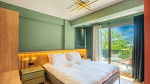 A modern bedroom with a large bed, wooden headboard, bedside lamps, and a view of a balcony with outdoor furniture. - Premium park apart (Kemer)