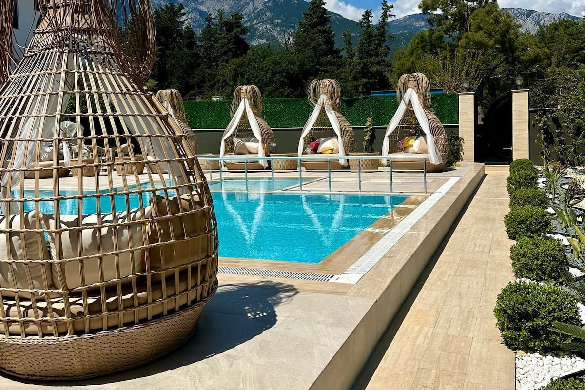 Zona de piscina con vista despejada a las montañas, una estructura tejida grande y un camino bordeado de arbustos.