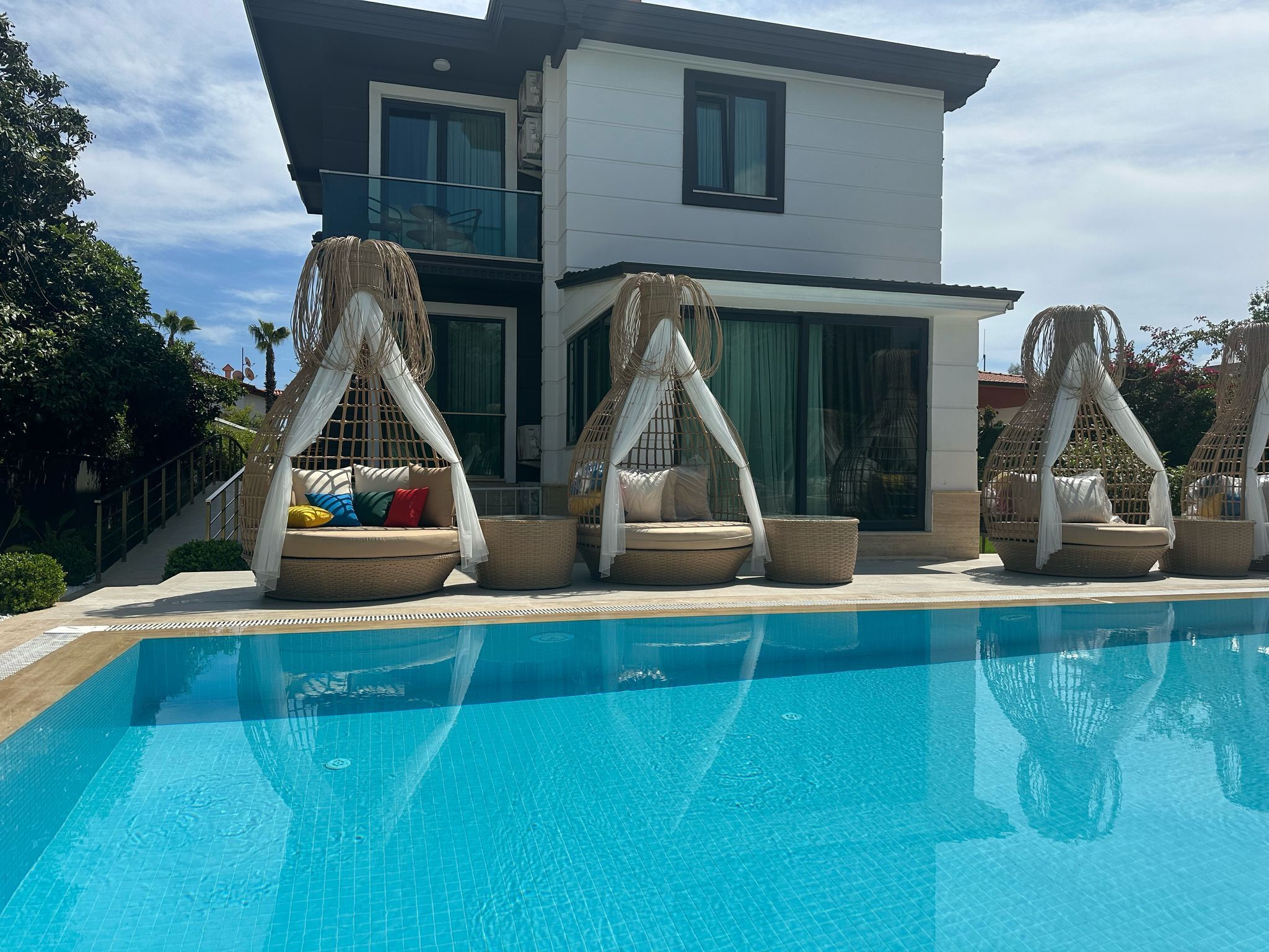 A modern house with a pool, outdoor seating, and a staircase leading to the entrance.