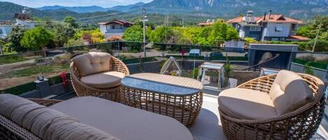 Un balcón con mobiliario de mimbre, una mesa de vidrio y vistas a montañas.