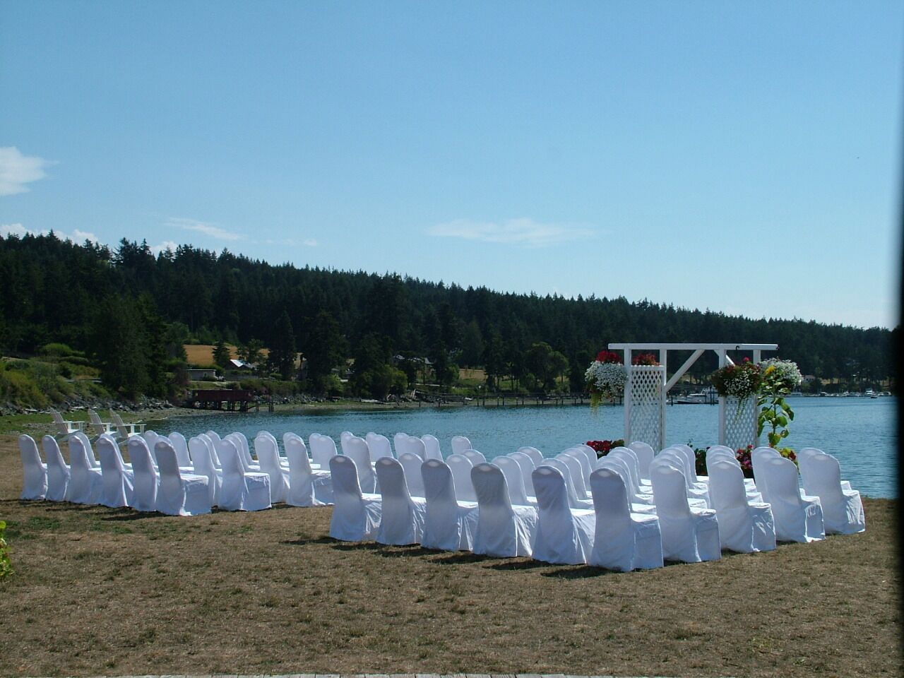 Una location sul lago con file di sedie bianche e un arco bianco.