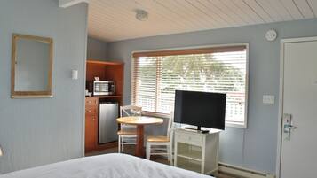 Une chambre d’hôtel comprenant un lit, un bureau avec une télévision, un petit coin cuisine et une fenêtre avec des stores.