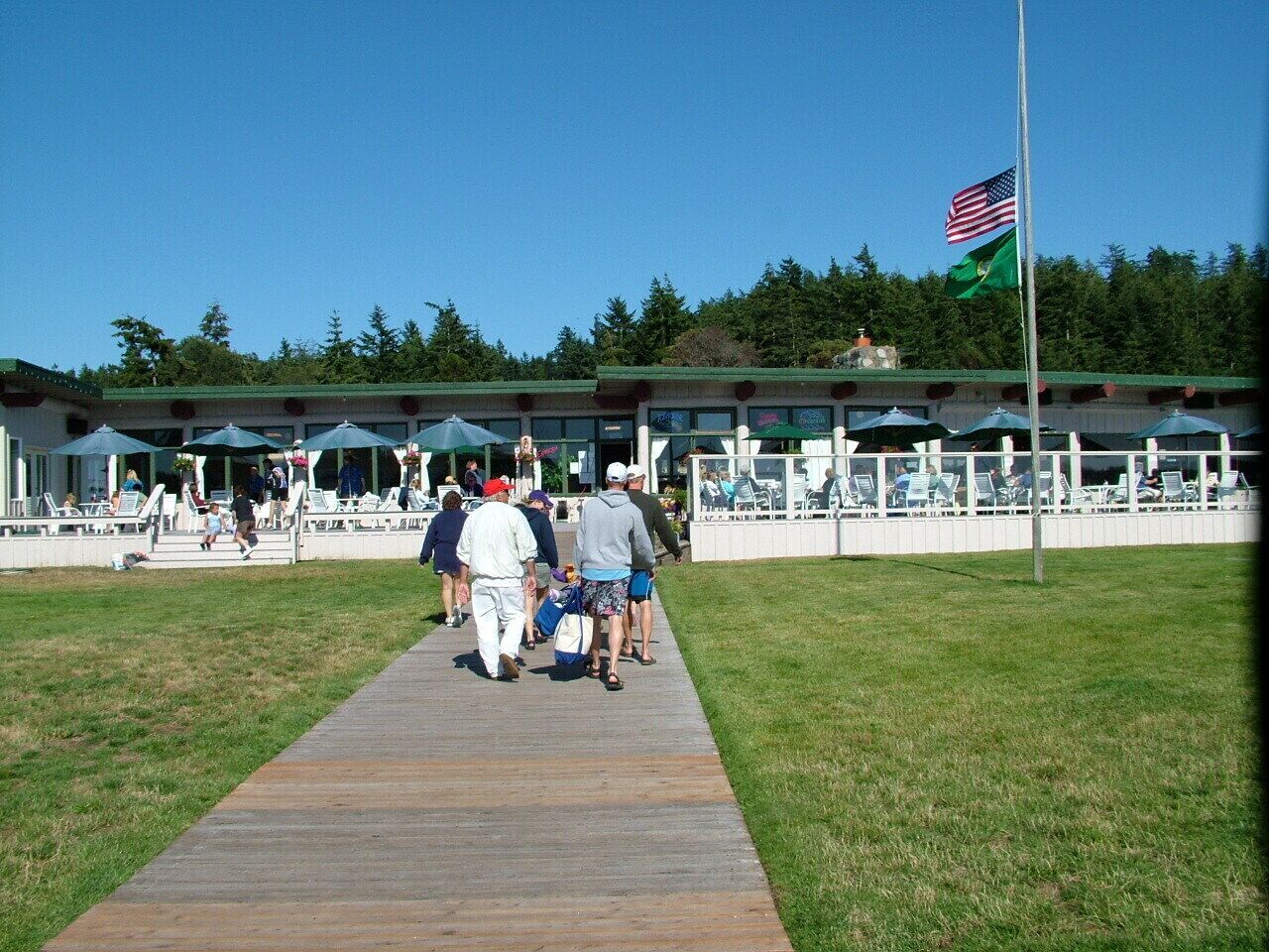 A wooden boardwalk leading to a building with outdoor seating and a flag.