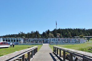 A wooden pier leading to a building with large windows and a flagpole.
