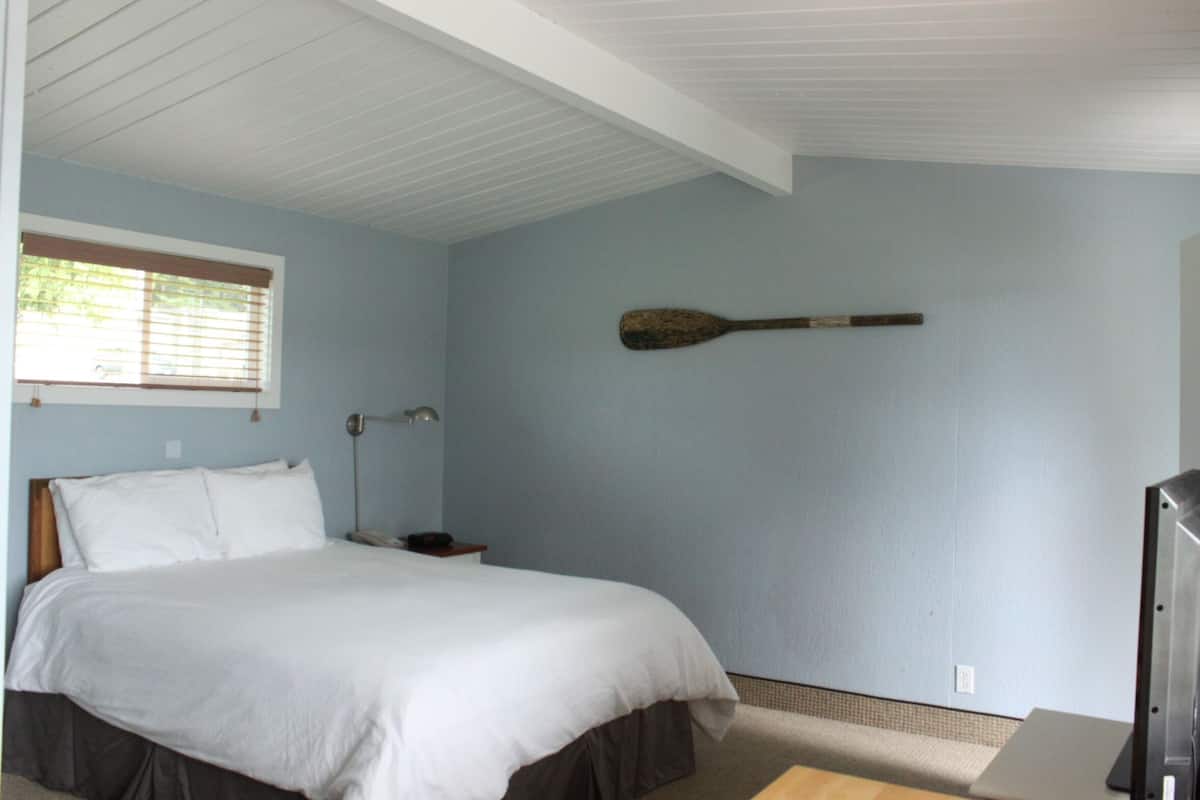Un dormitorio con una cama, una mesita de noche, una lámpara y un remo colgado en la pared.